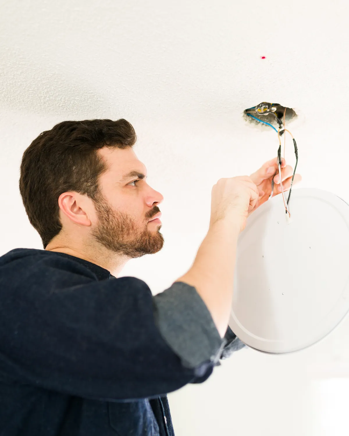 Electrician wiring a ceiling light fixture in a home